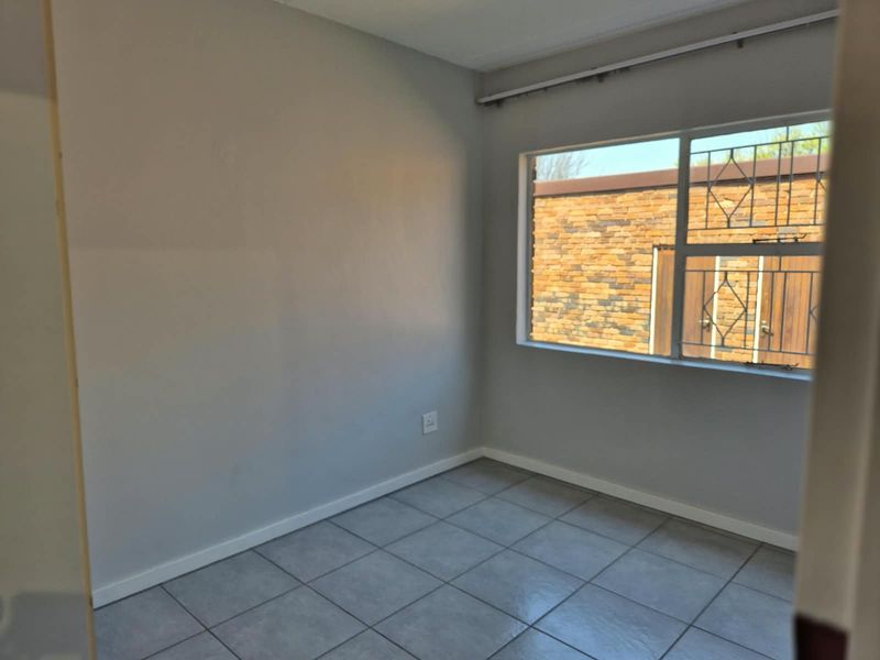 An empty bedroom featuring neutral grey walls, tiled flooring, and a window fitted with security bars.