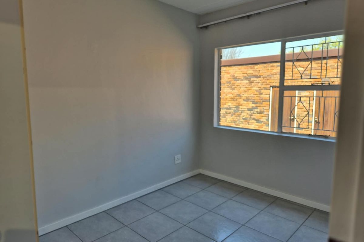 An empty bedroom featuring neutral grey walls, tiled flooring, and a window fitted with security bars.