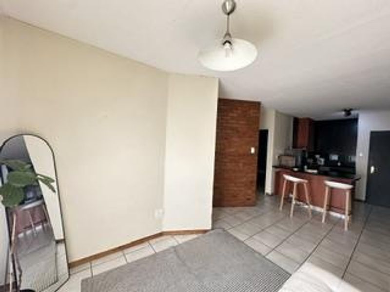 Open plan living area featuring tiled flooring, an exposed brick accent wall, and a functional kitchen with a breakfast bar.