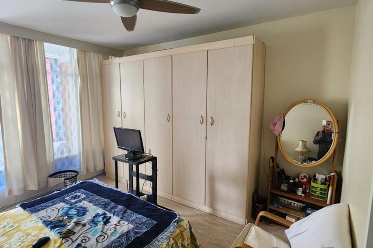 A bedroom featuring a large built-in wardrobe, ceiling fan, and wood-look laminate flooring, offering functional storage and a neutral base.