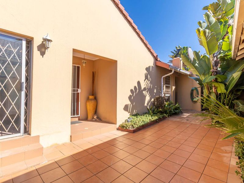 A covered patio area featuring tiled flooring, a sliding glass door with security gate, and a built-in planter box along the exterior wall.