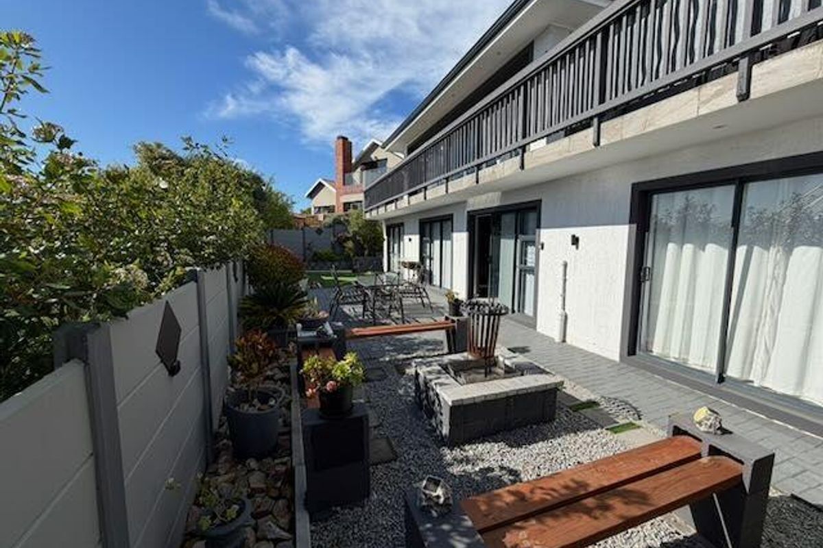 A well-maintained rear exterior area featuring a gravel courtyard, built-in fire pit, and direct access to the home via sliding glass doors.