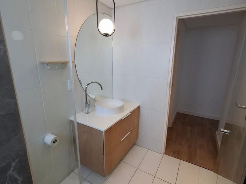 Modern bathroom featuring a floating timber vanity, vessel sink, round mirror, pendant lighting, and a glass-enclosed shower with neutral wall and floor tiling.