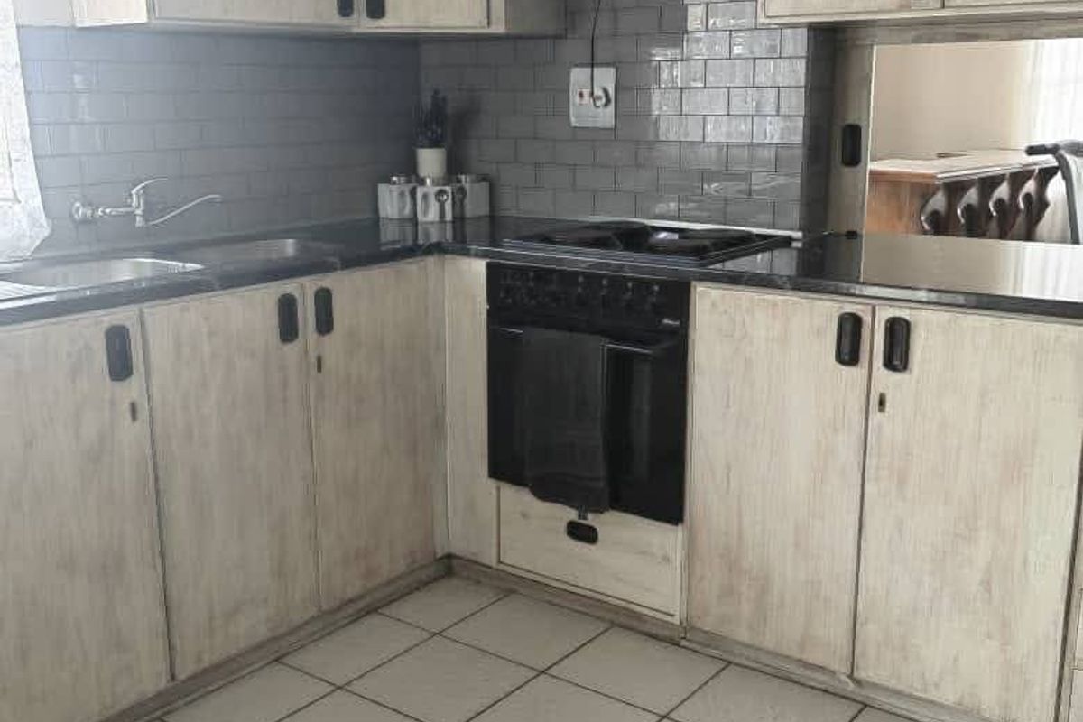 A functional kitchen featuring light-toned cabinetry, dark countertops, a subway tile backsplash, and a built-in oven with an extractor fan.