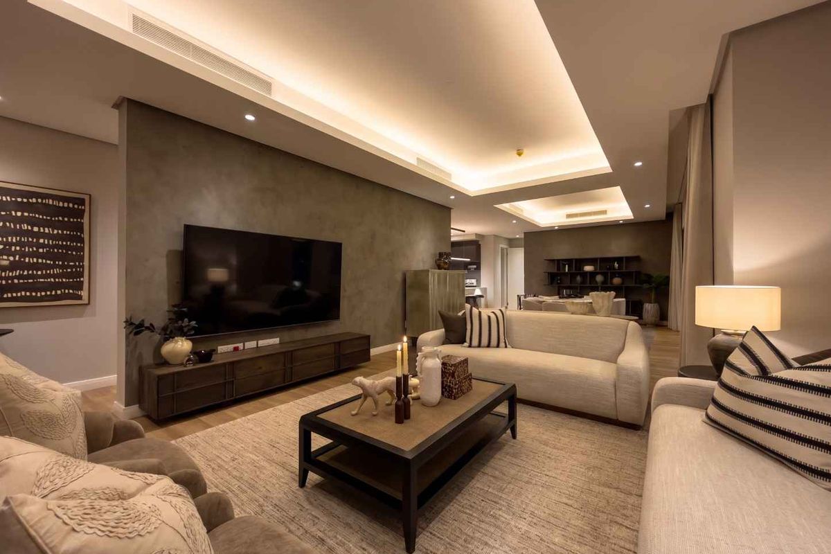 A modern, well-appointed living room featuring recessed ceiling lighting, ducted air conditioning, and a sophisticated feature wall with high-quality finishes.