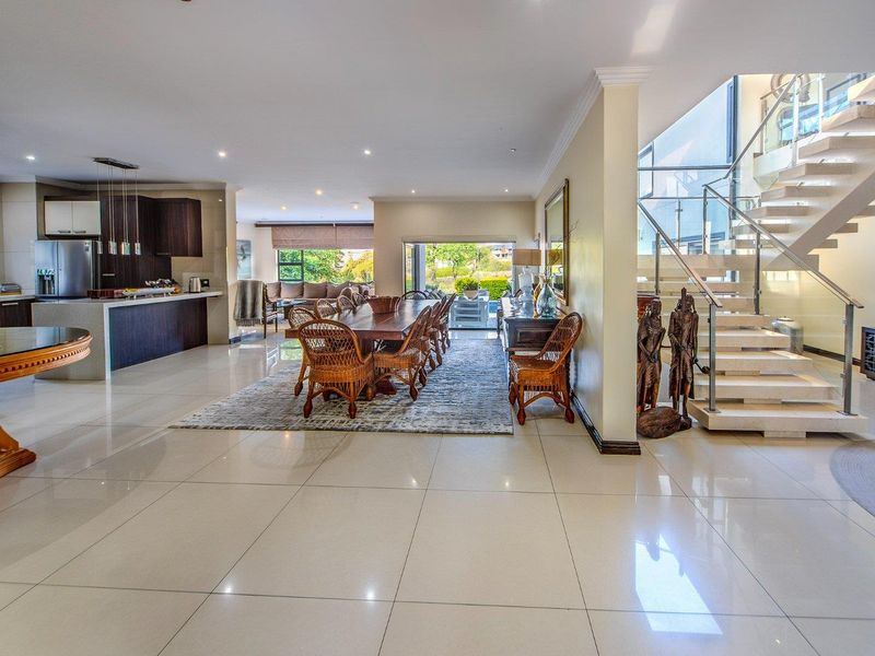Spacious open-plan living area featuring a modern kitchen, dining space, and a striking stone staircase with glass balustrade, leading to the upper level.