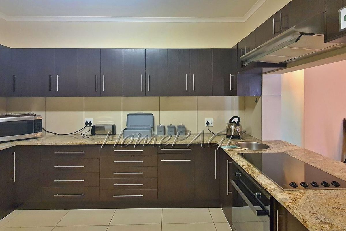 A functional kitchen featuring dark cabinetry, granite countertops, a built-in oven, and a glass cooktop, providing ample storage and workspace.