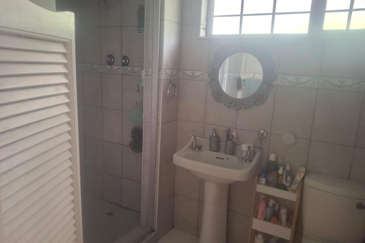 A functional bathroom featuring a pedestal basin, shower enclosure, and tiled finishes, illuminated by a grid-style window.
