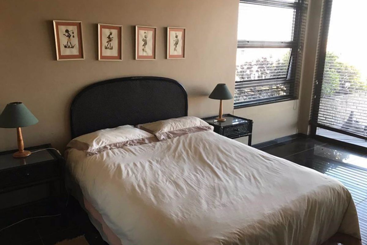 A bedroom featuring dark tiled flooring, large windows with blinds, and access to an outdoor area.