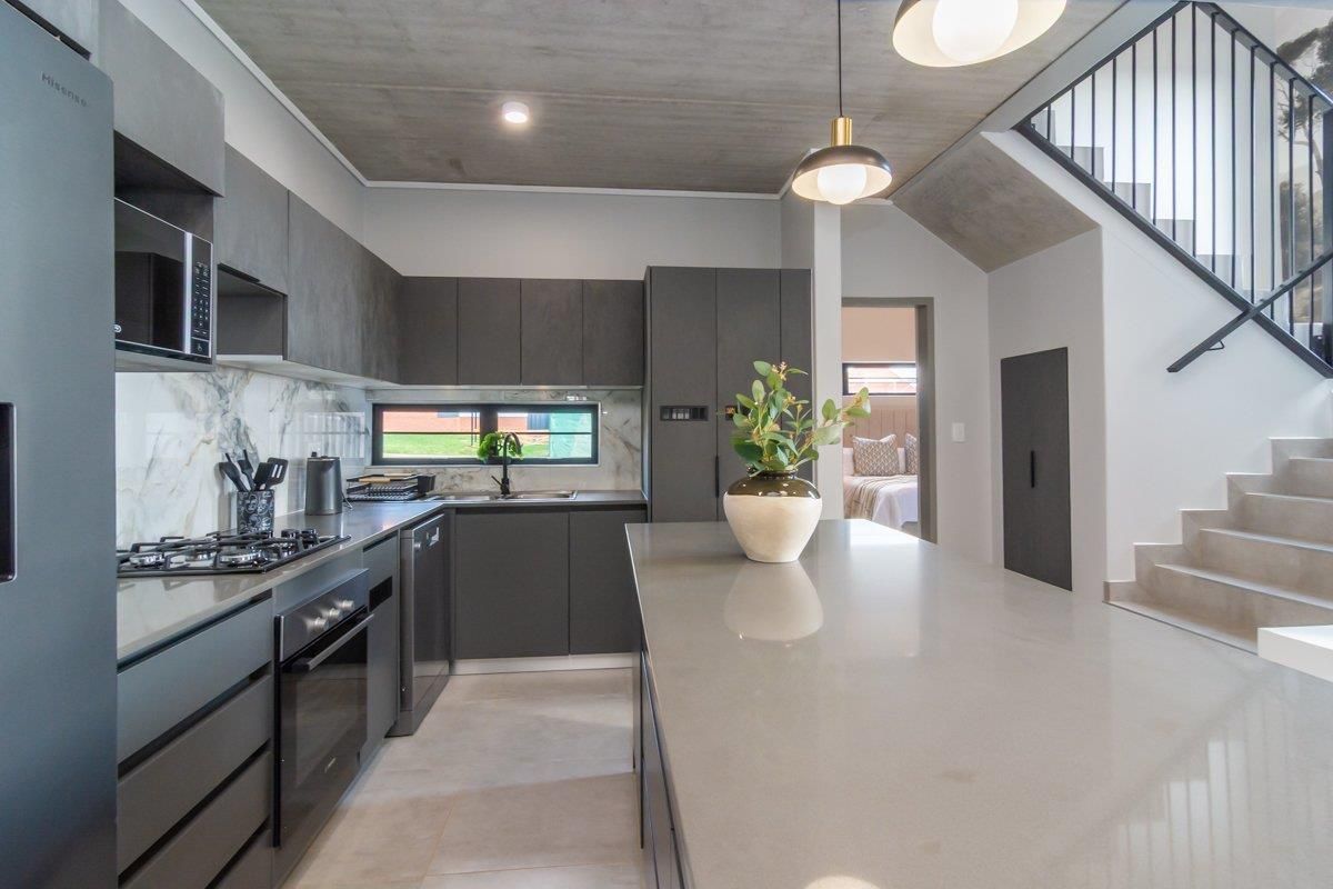 Modern kitchen featuring dark cabinetry, stone countertops, a central island, and an exposed concrete ceiling, adjacent to a staircase.