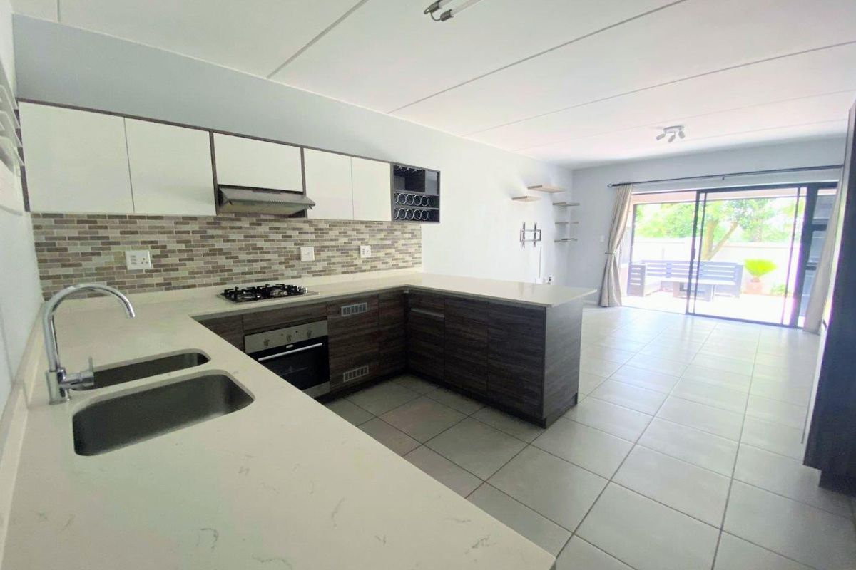Spacious open-plan kitchen and living area featuring modern cabinetry, stone countertops, gas hob, and large sliding doors leading to an outdoor patio.
