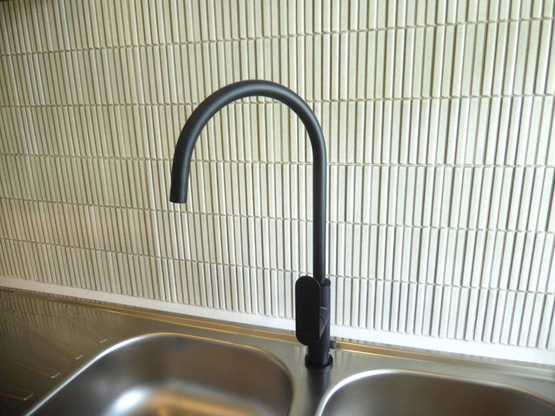 A modern kitchen sink area featuring a sleek matte black gooseneck mixer tap and a contemporary textured vertical tile splashback.