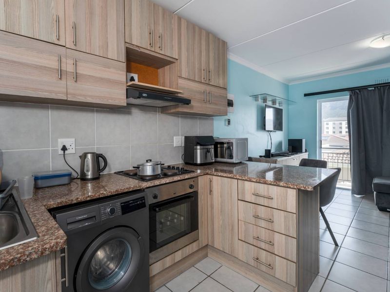 Open-plan kitchen featuring wood-look cabinetry, granite countertops, built-in oven, and hob, flowing into a living area with access to a balcony.
