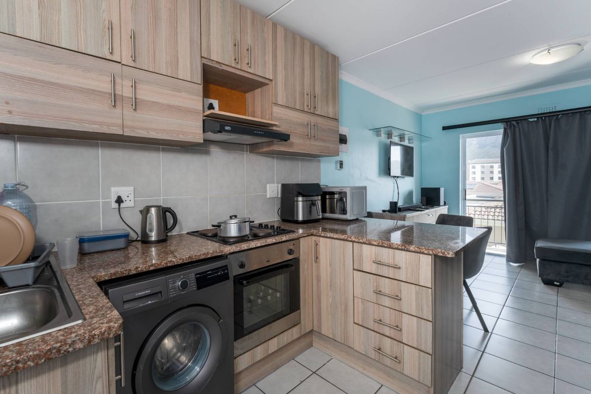 Open-plan kitchen featuring wood-look cabinetry, granite countertops, built-in oven, and hob, flowing into a living area with access to a balcony.
