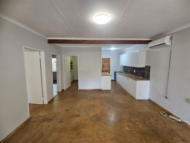An open-plan living and kitchen area featuring polished concrete floors, white cabinetry, and an air conditioning unit, offering a clean, versatile space.