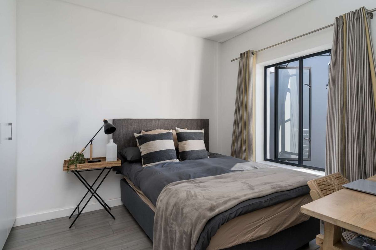 A bright and modern bedroom featuring neutral walls, grey wood-look flooring, and a large window with dark frames.