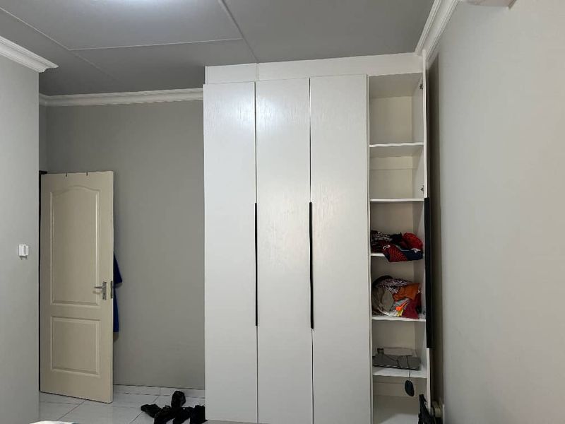 A bedroom featuring a modern white built-in wardrobe with black handles, tiled flooring, and crown molding detail.