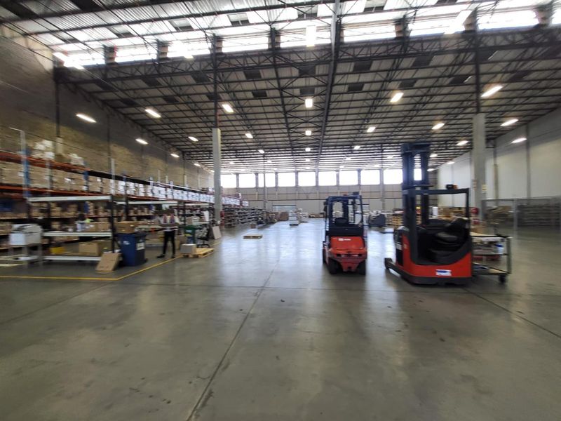 Spacious industrial warehouse featuring high ceilings, exposed steel trusses, polished concrete flooring, and extensive built-in metal racking systems for storage.