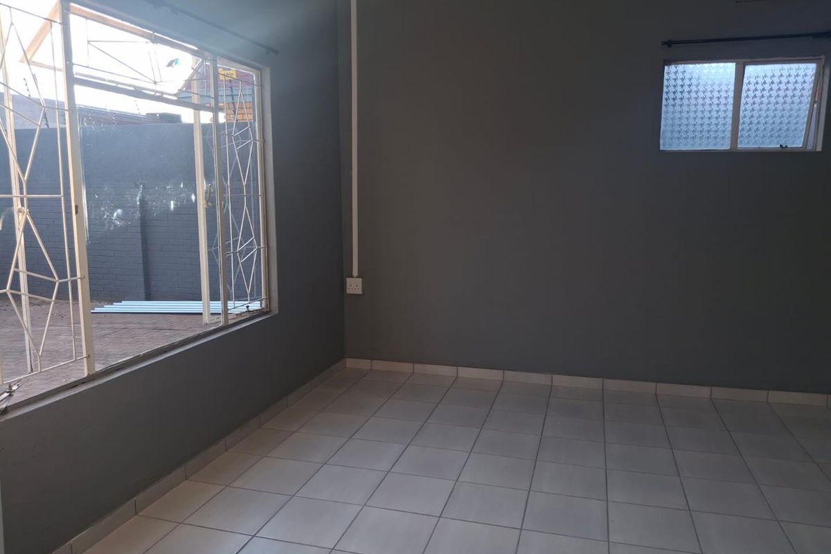 An empty living room featuring neutral grey walls, tiled flooring, and security bars on the windows, offering a clean and versatile space.