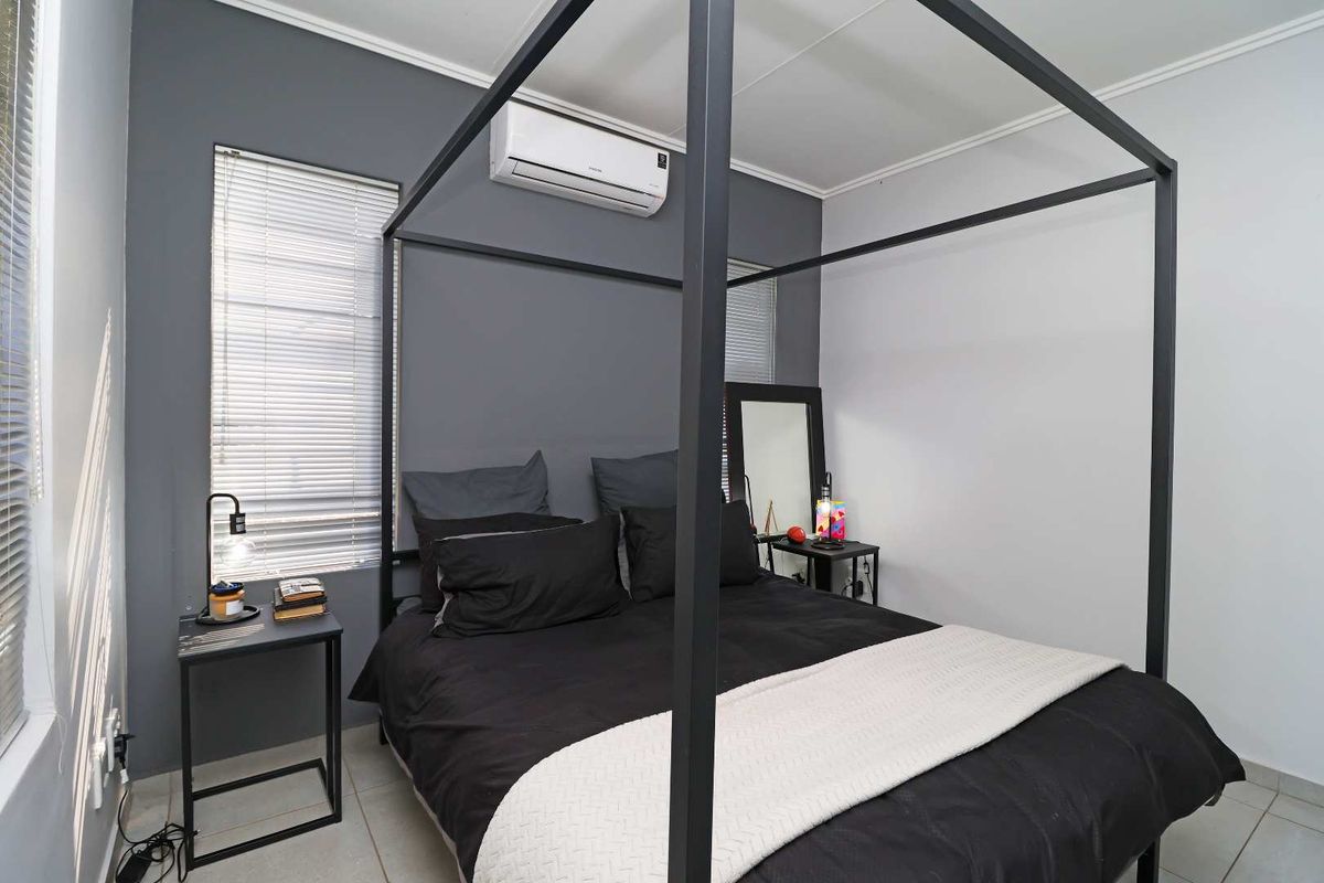A well-maintained bedroom featuring tiled flooring, a wall-mounted air conditioning unit, and dual windows with fitted blinds.