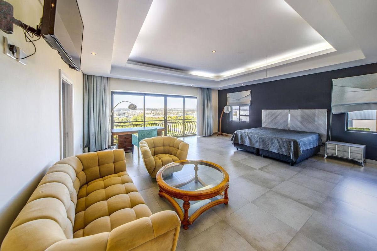 Spacious bedroom featuring a recessed tray ceiling with integrated lighting, large sliding glass doors leading to a balcony, and neutral floor tiling.