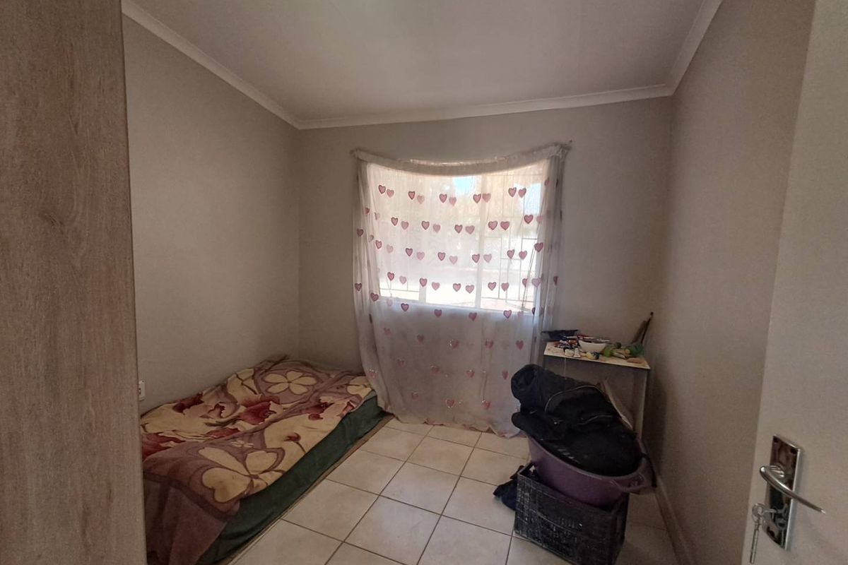 A compact bedroom featuring neutral wall paint, tiled flooring, and a window with natural light.