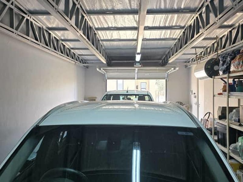 A spacious garage featuring exposed steel roof trusses, functional lighting, and a sectional garage door, providing secure parking and storage space.