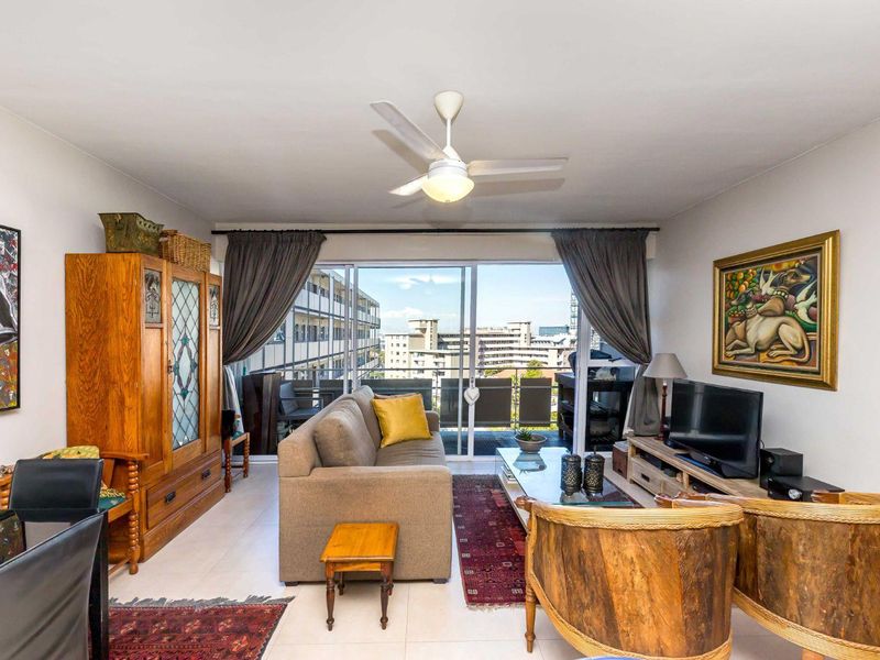 A well-lit living room featuring tiled flooring, a ceiling fan, and large sliding glass doors that open onto a balcony with urban views.