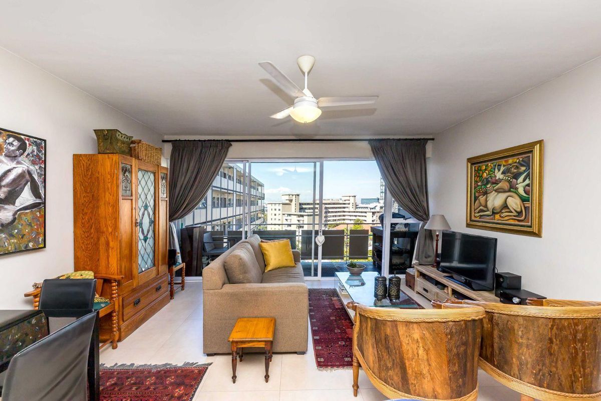 A well-lit living room featuring tiled flooring, a ceiling fan, and large sliding glass doors that open onto a balcony with urban views.