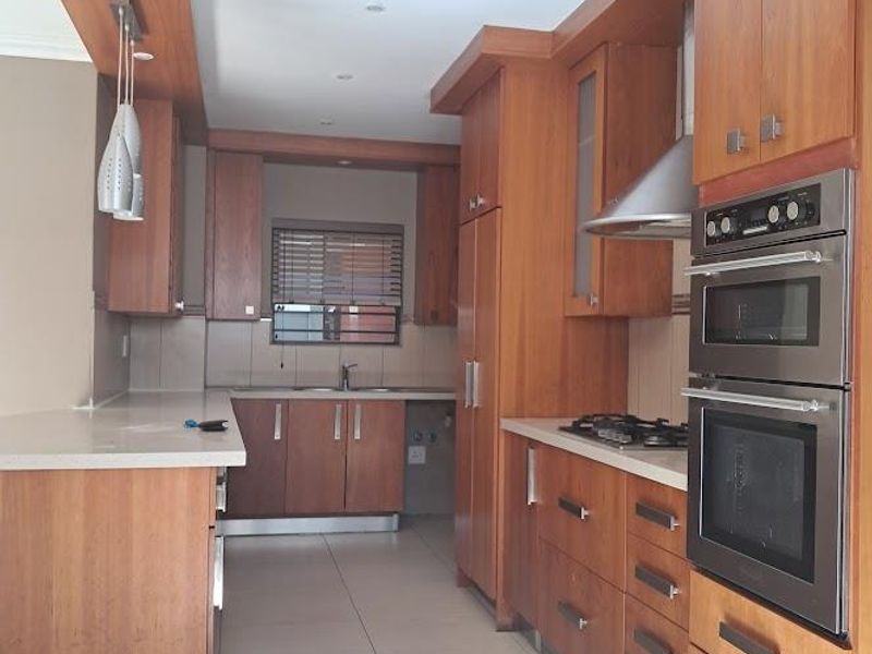 A well-maintained kitchen featuring warm-toned wooden cabinetry, stone countertops, integrated stainless steel appliances, and tiled flooring in a clean, functional layout.