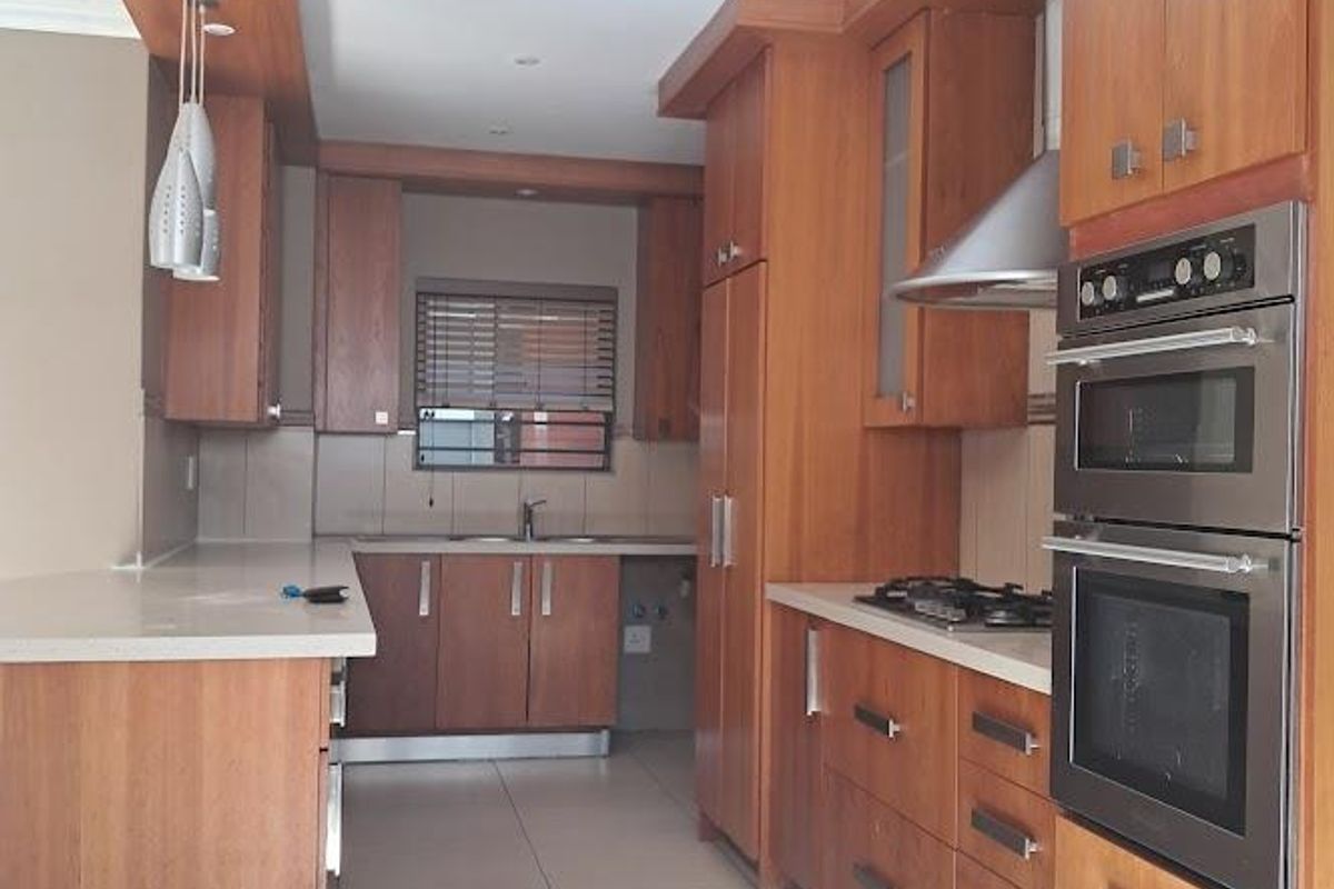 A well-maintained kitchen featuring warm-toned wooden cabinetry, stone countertops, integrated stainless steel appliances, and tiled flooring in a clean, functional layout.