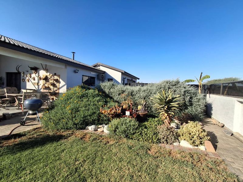 A well-maintained rear exterior view featuring a paved patio area, established garden beds with succulents, and a neat lawn.