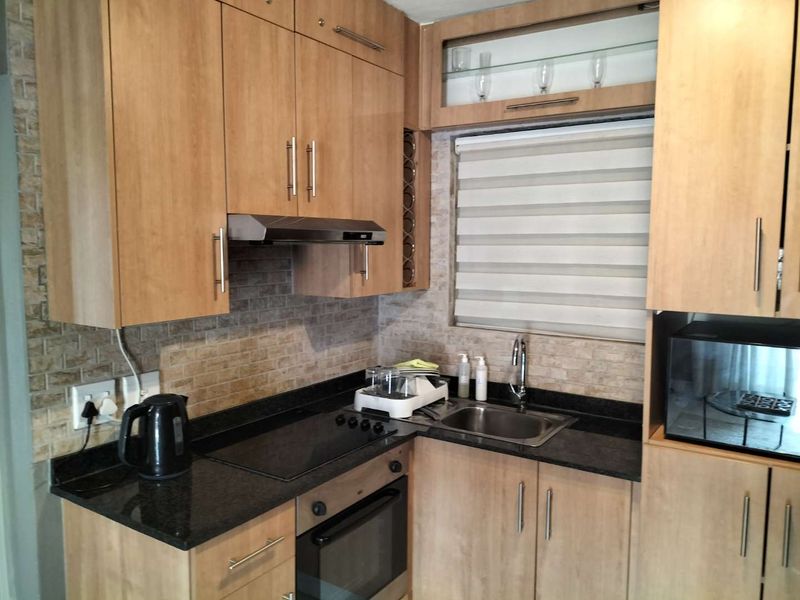 A functional kitchen featuring light wood cabinetry, granite countertops, a built-in oven, electric hob, and a tiled backsplash with a window.