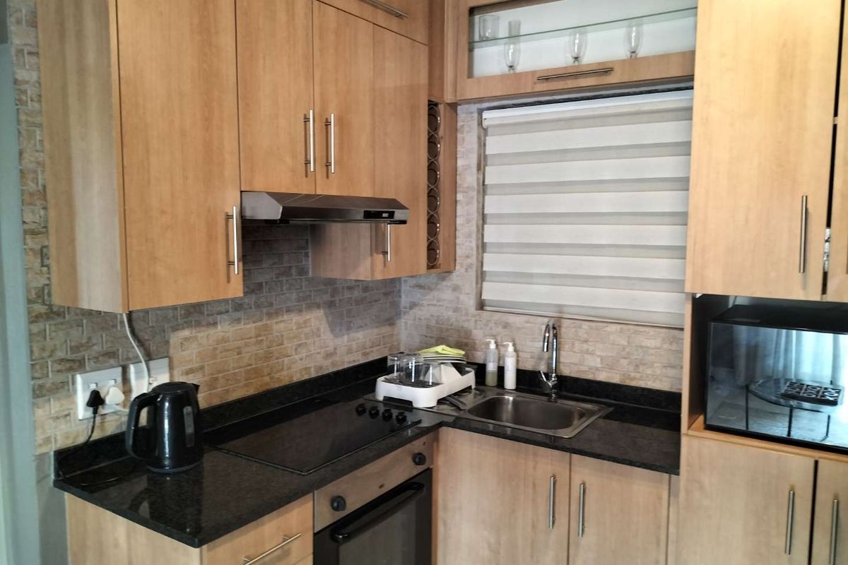 A functional kitchen featuring light wood cabinetry, granite countertops, a built-in oven, electric hob, and a tiled backsplash with a window.