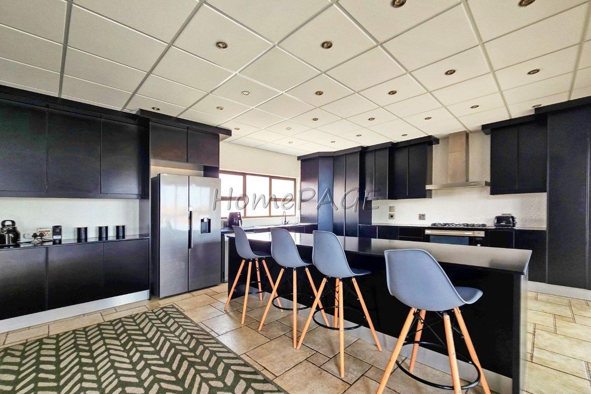Spacious kitchen featuring dark cabinetry, a large central island with breakfast bar seating, integrated appliances, and tiled flooring.