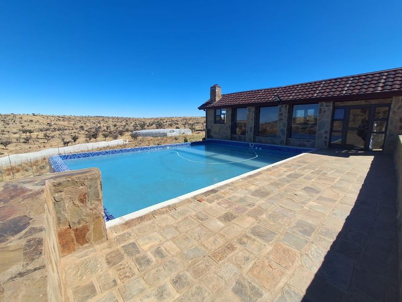 Outdoor pool area featuring a tiled patio, stone-clad building exterior, and a swimming pool overlooking the surrounding landscape.