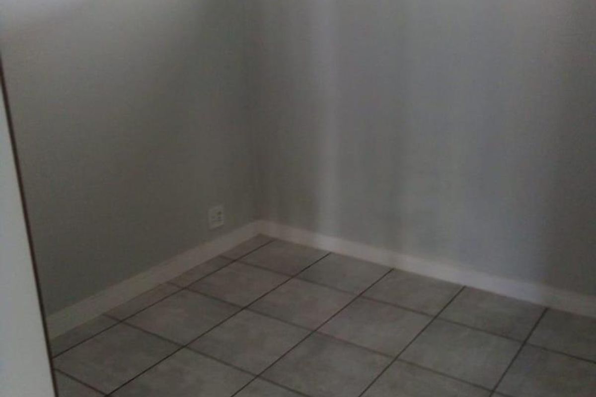 A small, empty room featuring neutral grey floor tiles, white walls, and a high-set horizontal window providing natural light.