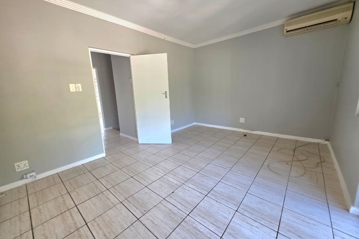 A spacious, empty living room featuring neutral tiled flooring, crown molding, and a wall-mounted air conditioning unit.