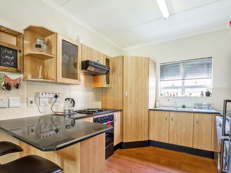 A functional kitchen featuring light wood-finish cabinetry, dark granite countertops, a built-in oven with gas hob, and a stainless steel sink.