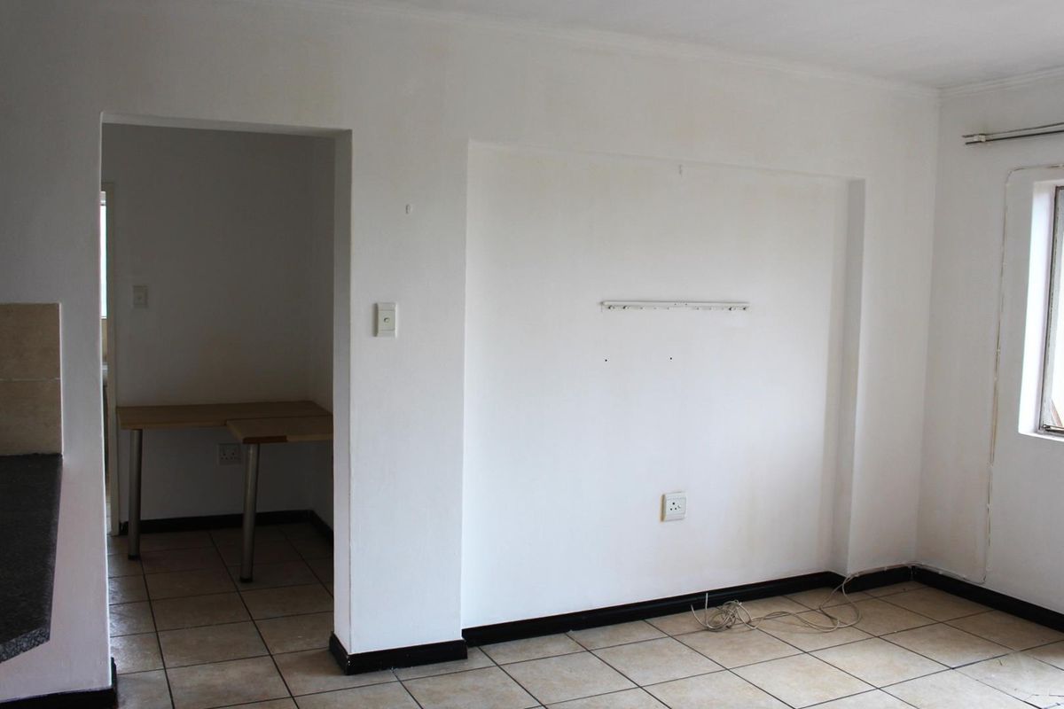 An empty living area featuring tiled flooring, a recessed wall section, and an adjacent utility space with a built-in desk.