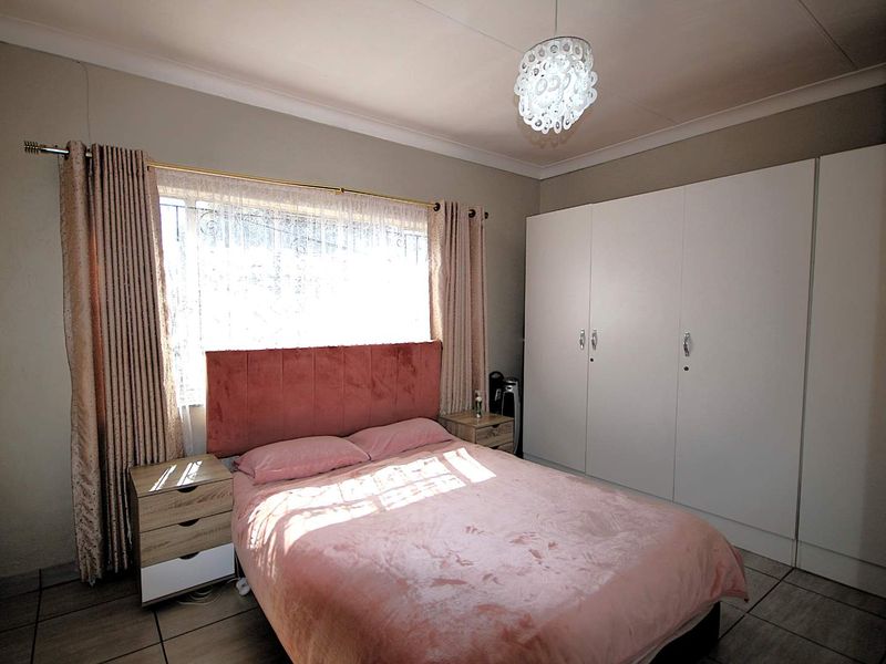 A well-lit bedroom featuring built-in cupboards, tiled flooring, and security bars on the window, providing a functional and comfortable living space.
