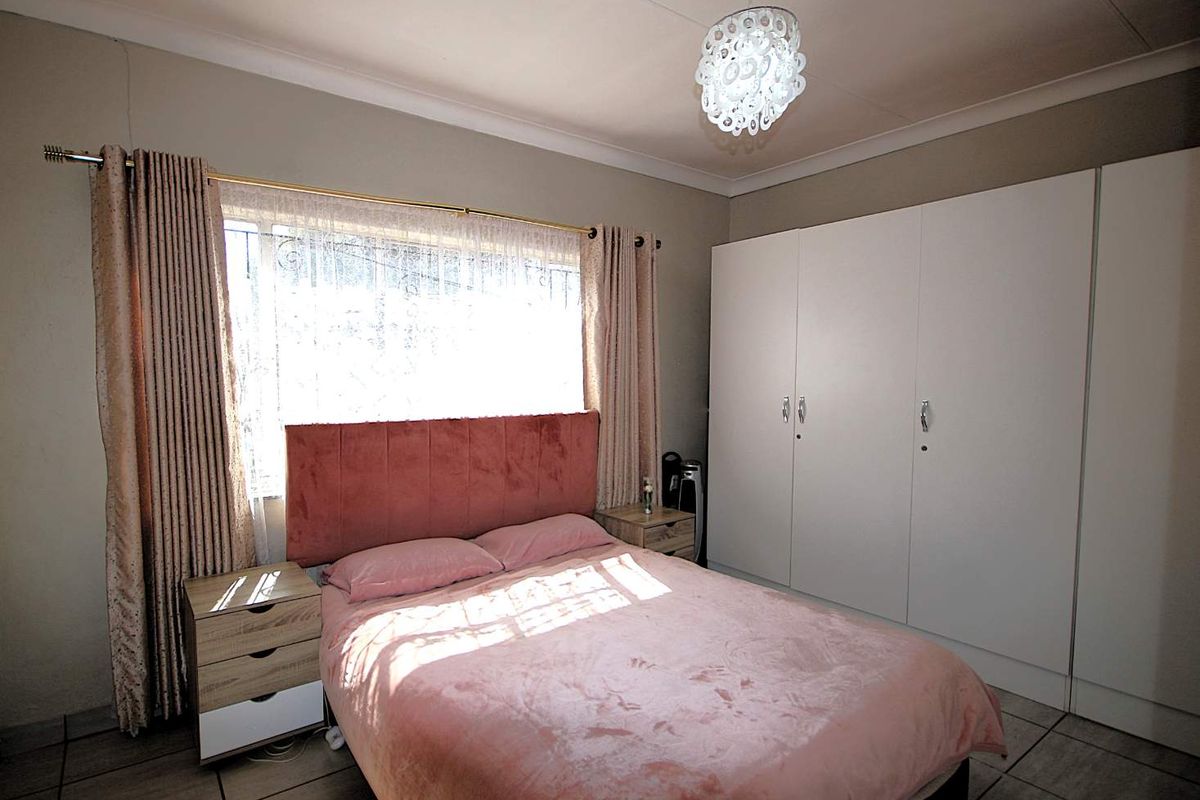 A well-lit bedroom featuring built-in cupboards, tiled flooring, and security bars on the window, providing a functional and comfortable living space.