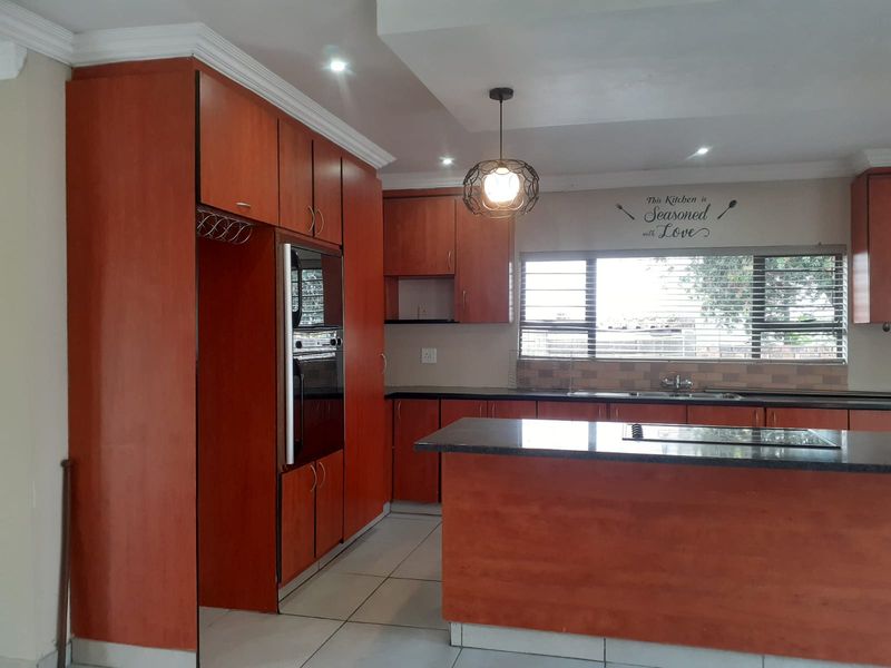 A functional kitchen featuring warm-toned built-in cabinetry, granite countertops, a central island with a cooktop, and tiled flooring with ample natural light.