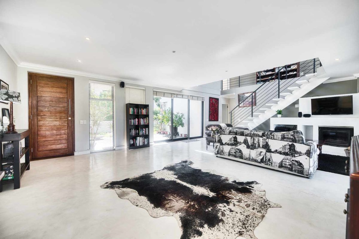 Spacious open-plan living area featuring polished concrete floors, a modern staircase with metal balustrade, a fireplace, and large sliding doors leading to the exterior.