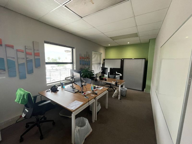 A functional office space featuring a suspended ceiling, recessed lighting, carpeted flooring, and a large wall-mounted whiteboard.