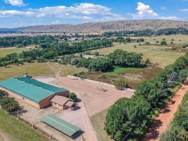 Aerial view of a commercial property featuring a large warehouse building, a carport, and expansive surrounding land with established trees and rural access.