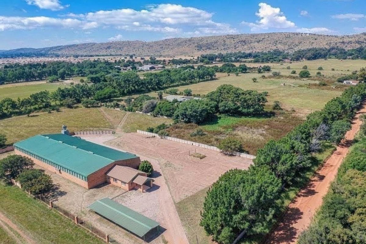 Aerial view of a commercial property featuring a large warehouse building, a carport, and expansive surrounding land with established trees and rural access.