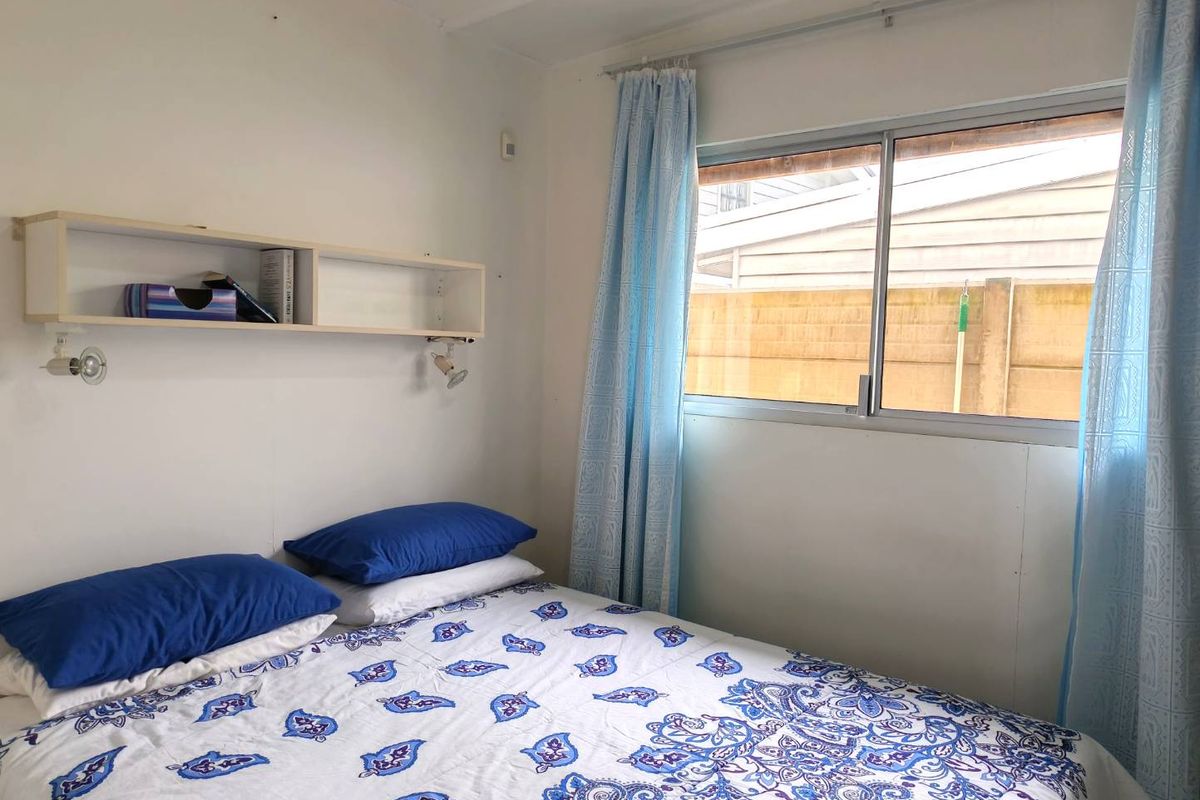 A functional bedroom featuring a sliding window and wall-mounted shelving unit, providing a simple and practical living space.