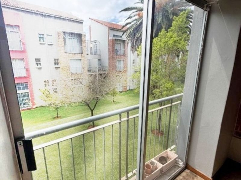 A view from an interior room through a sliding glass door onto a balcony overlooking a communal garden area.