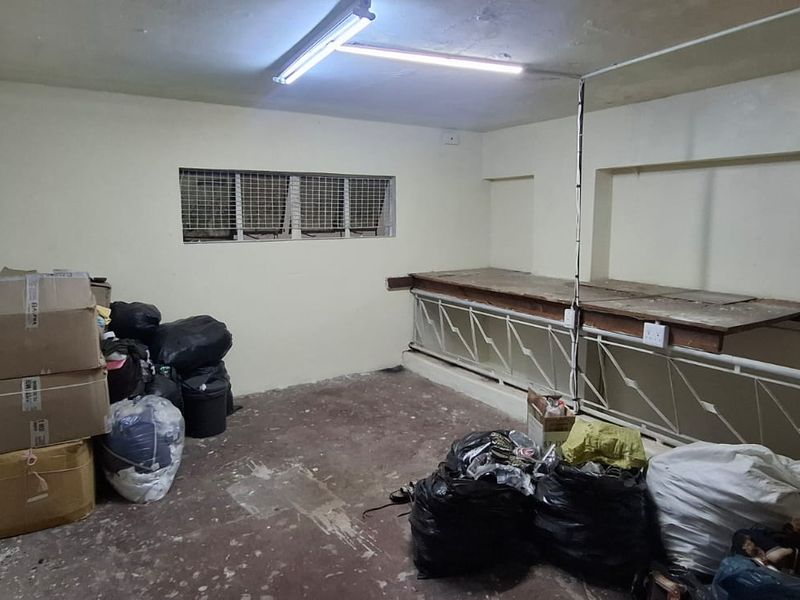 A utilitarian storage or workspace area featuring a built-in workbench, security-grille window, and basic fluorescent lighting, currently used for storage.